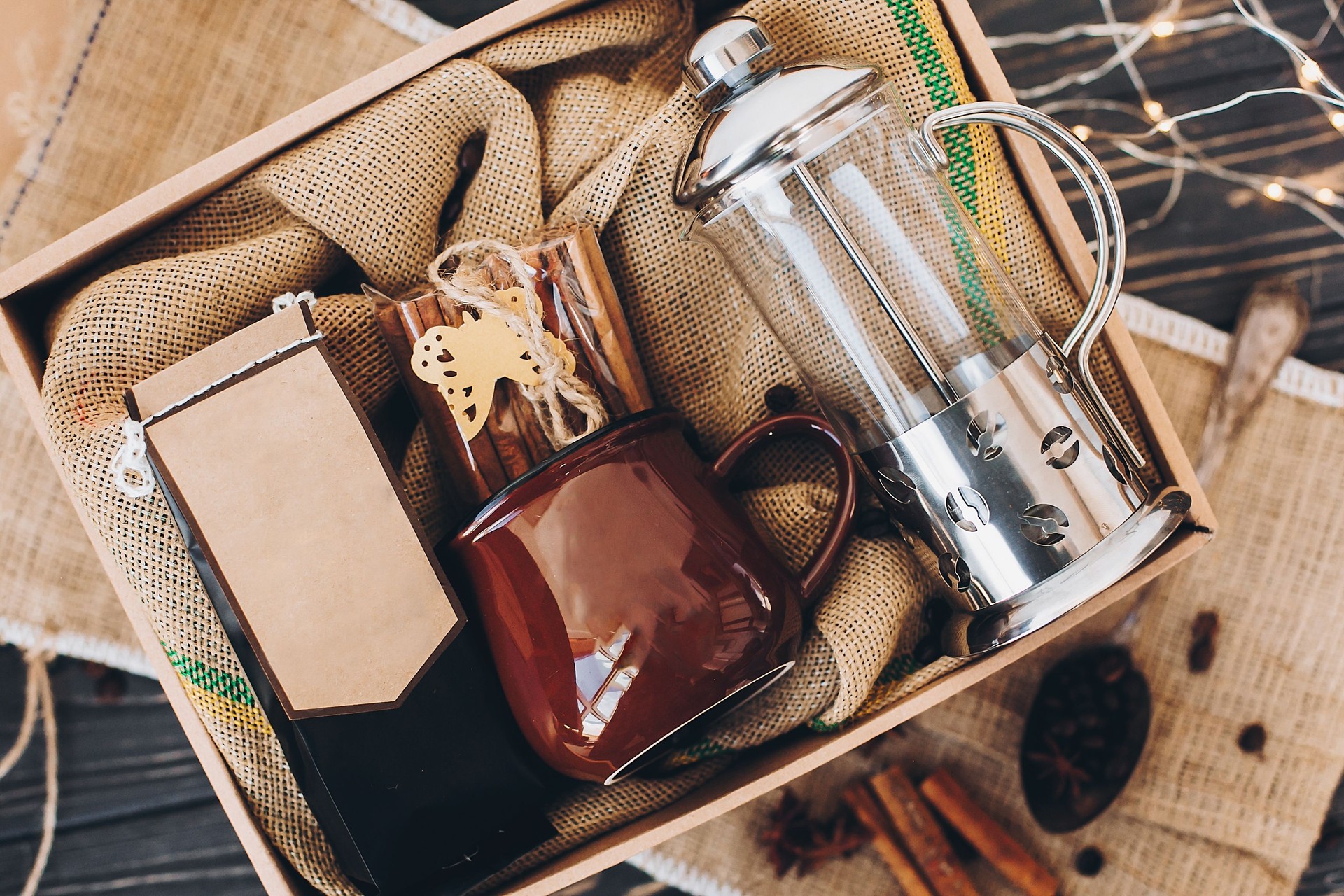 Gift box with coffee set. Coffee, cup, cinnamon, press on burlap in box on table, top view
