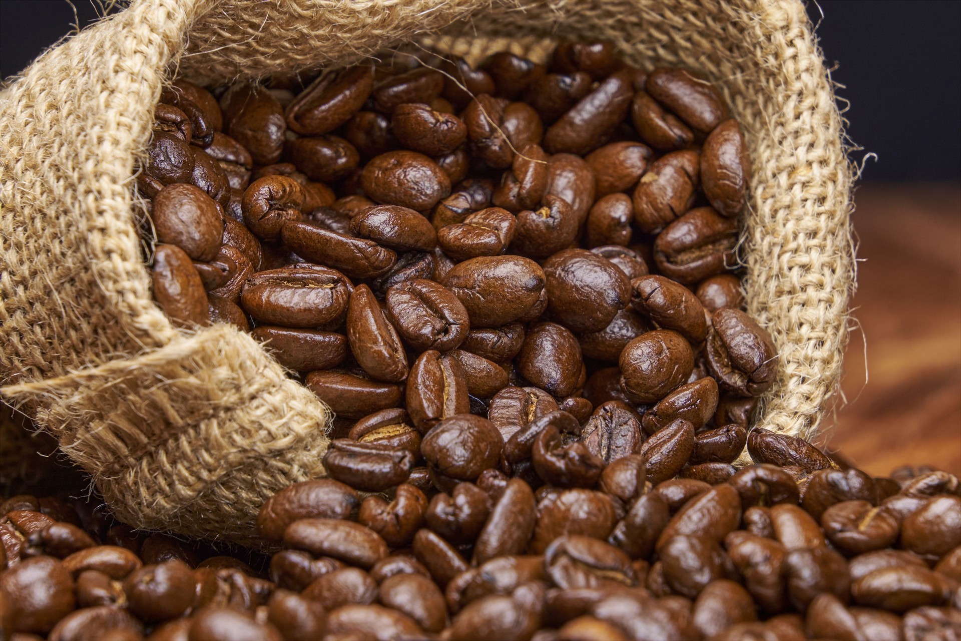 Dark roasted coffee beans in a jute bag on a wooden table