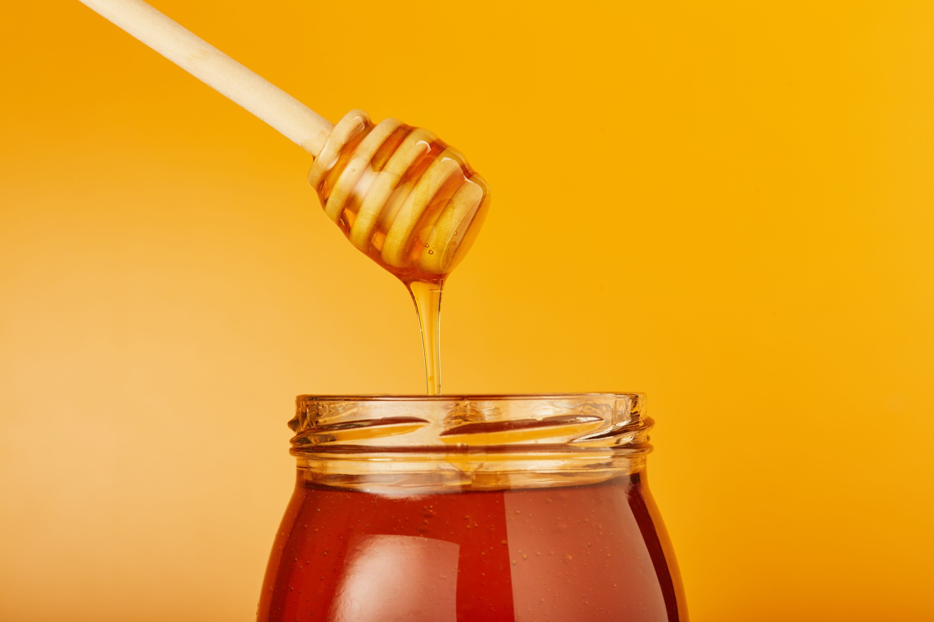 Honey dripping from wooden honey dipper in to jar